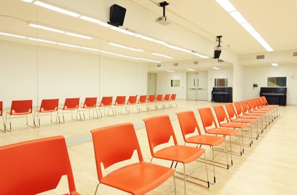 Spacious dance room lined with chairs and a grand piano