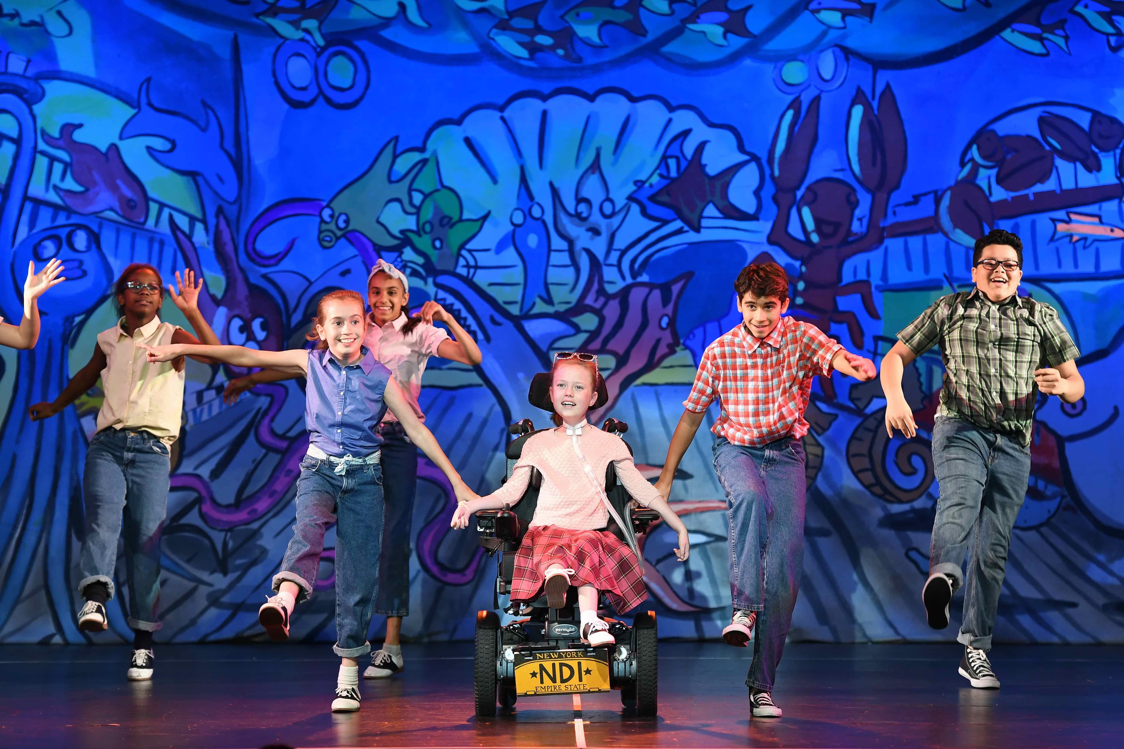 girl in a wheelchair dancing with three kids on a stage